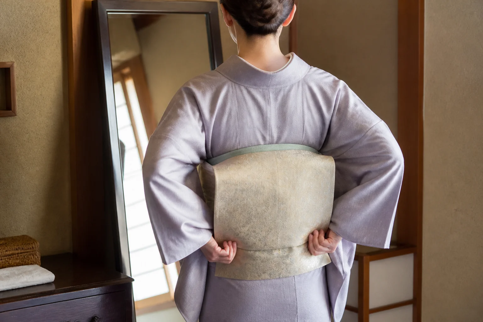 鏡の前で背中のしわを脇に寄せ、帯揚げと衿元を整えている着物の後ろ姿の写真